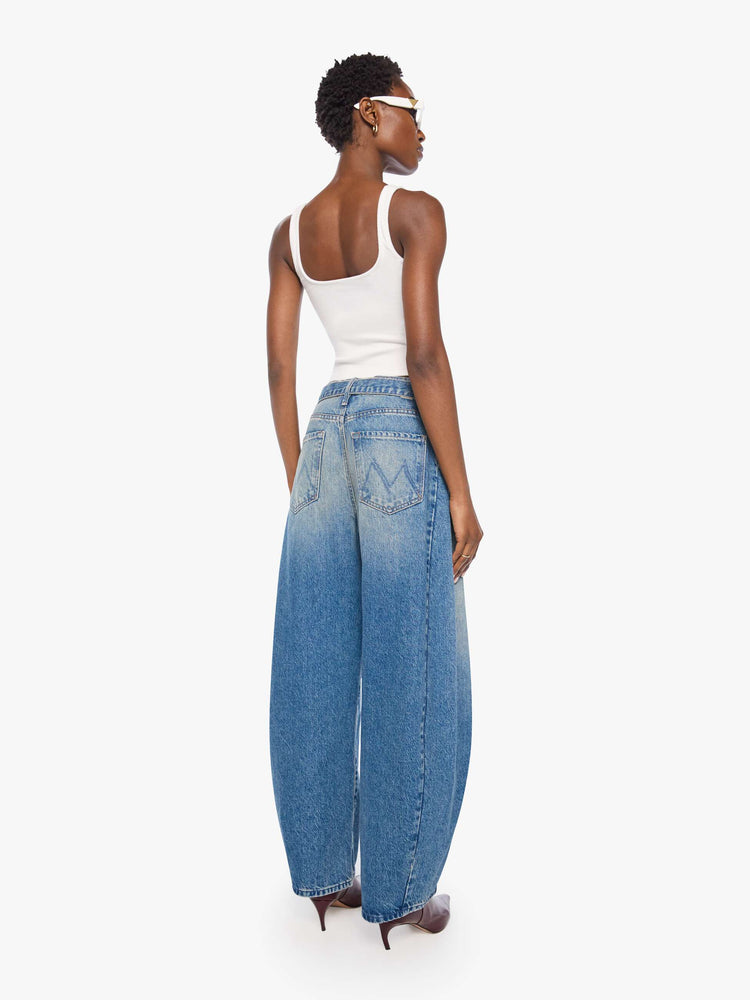 Back view of a woman in a mid blue wide leg super high-waisted jeans are designed with a belted waistband, zip fly, an inset panel on the outer seam, slightly tapered leg and a clean hem.