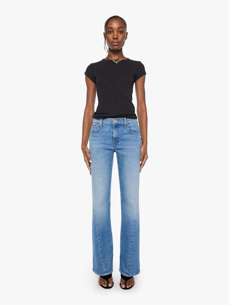 Front view of a woman in a mid blue mid-rise bootcut with a zip fly, looser leg, twisted outer seam and a long 31-inch inseam with a clean hem.