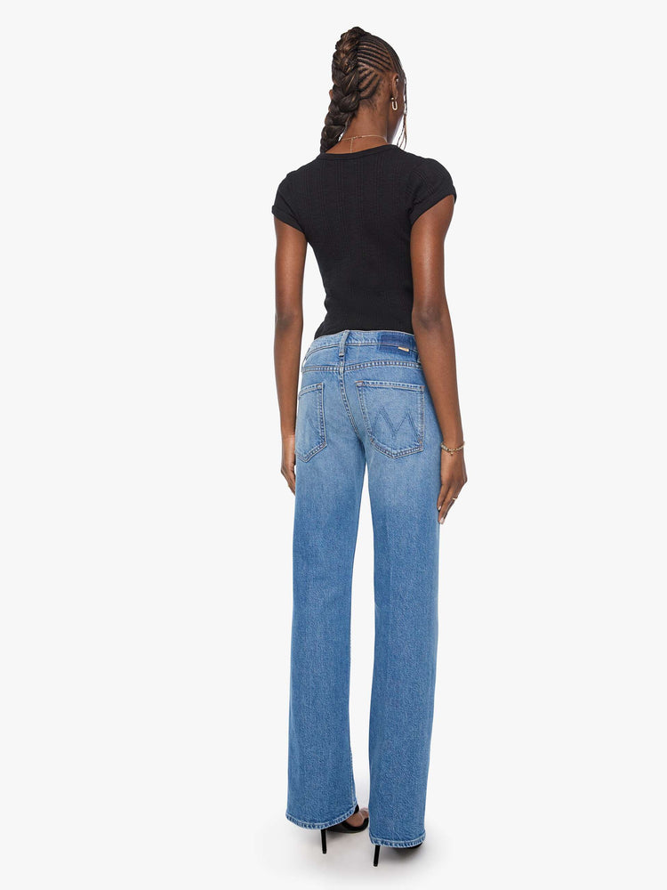 Back view of a woman in a mid blue mid-rise bootcut with a zip fly, looser leg, twisted outer seam and a long 31-inch inseam with a clean hem.