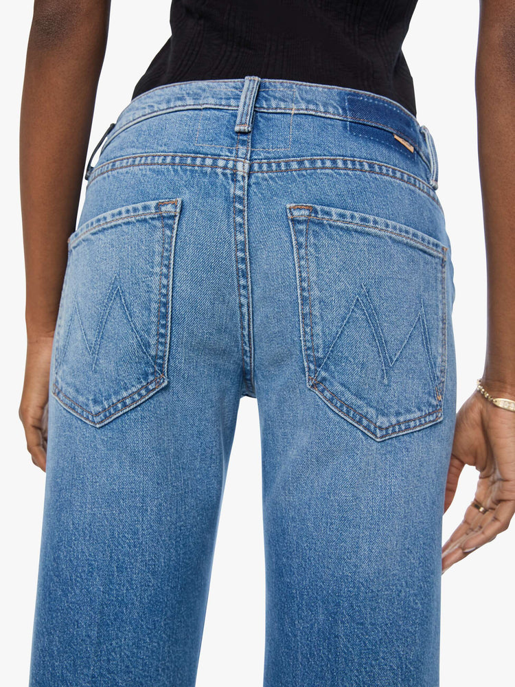 Close up view of a woman in a mid blue mid-rise bootcut with a zip fly, looser leg, twisted outer seam and a long 31-inch inseam with a clean hem.