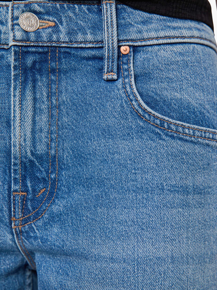 Swatch view of a woman in a mid blue mid-rise bootcut with a zip fly, looser leg, twisted outer seam and a long 31-inch inseam with a clean hem.