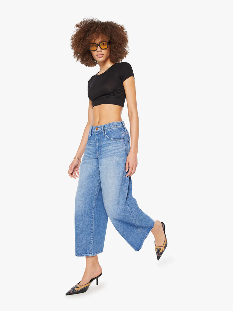 Walking  view of a woman in a med blue  high-waisted jeans have a low-slung fit, zip fly, loose wide-leg and a 28.5-inch inseam with a clean hem. 