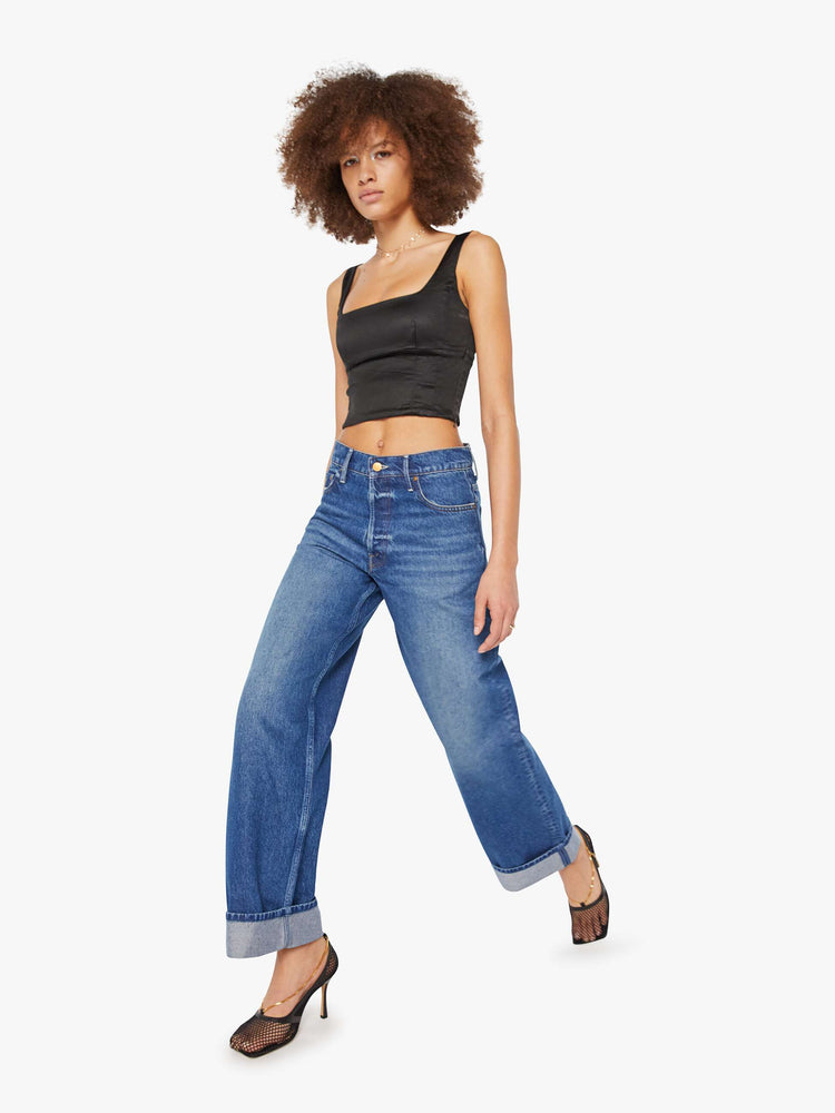 Walking view of a woman in mid blue wide straight-leg jeans designed to sit on the hips with a slouchy fit, button-fly and a long 31-inch inseam with a cuffed hem.