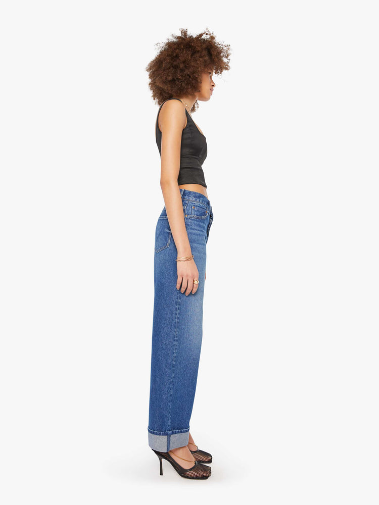 Side view of a woman in mid blue wide straight-leg jeans designed to sit on the hips with a slouchy fit, button-fly and a long 31-inch inseam with a cuffed hem.
