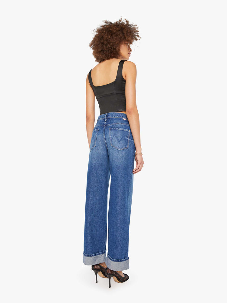 Back view of a woman in mid blue wide straight-leg jeans designed to sit on the hips with a slouchy fit, button-fly and a long 31-inch inseam with a cuffed hem.