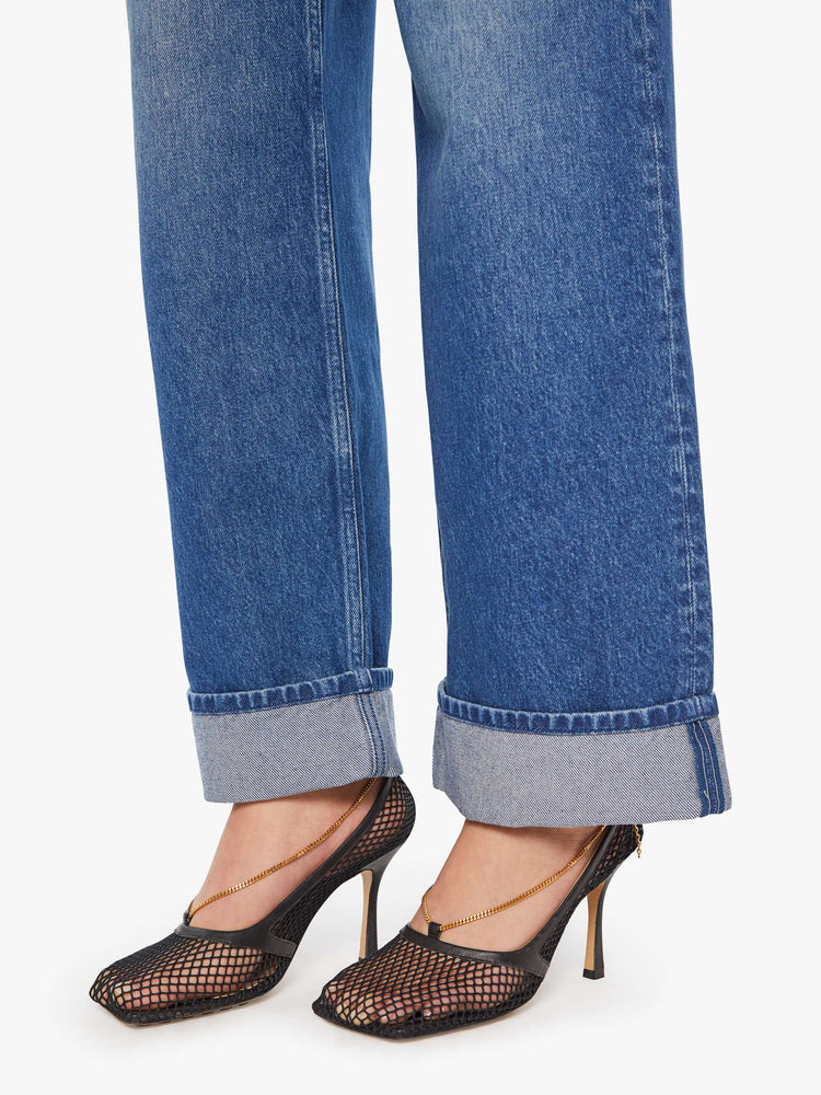 Hem view of a woman in mid blue wide straight-leg jeans designed to sit on the hips with a slouchy fit, button-fly and a long 31-inch inseam with a cuffed hem.