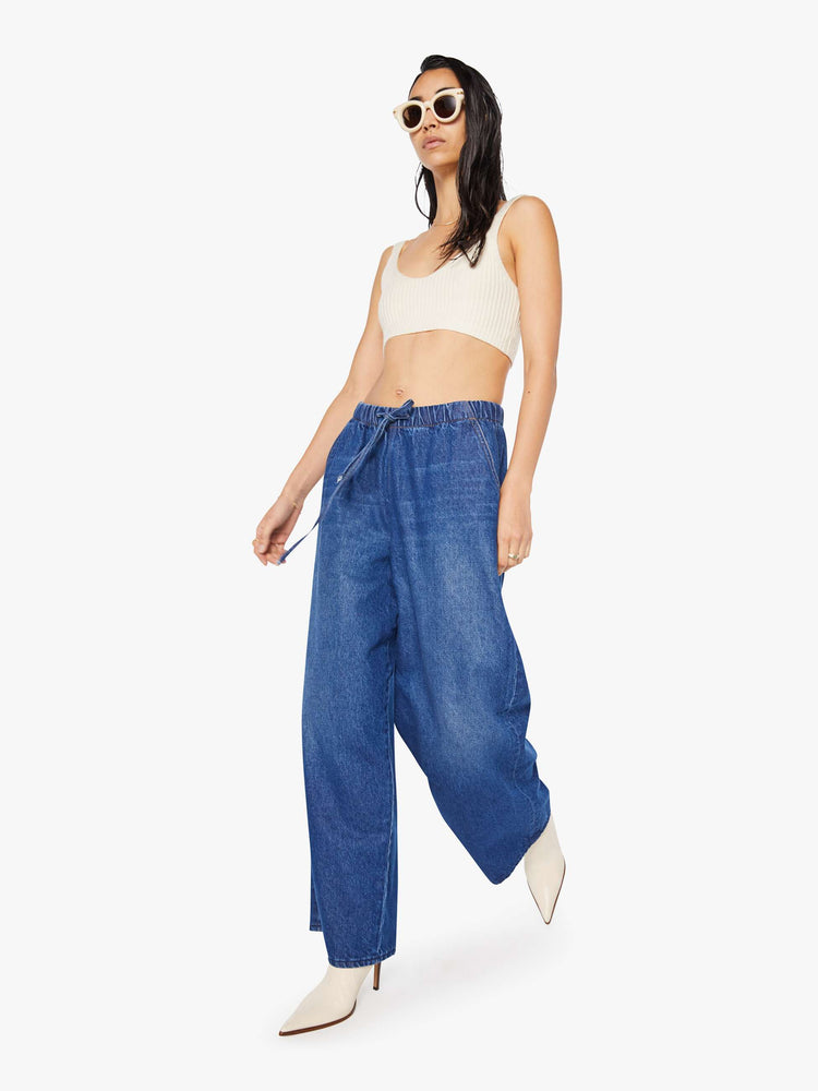 Walking view of a woman in a super high-waisted jeans have a loose straight leg, elastic drawstring waistband, zip fly and a 30-inch inseam with a clean hem.