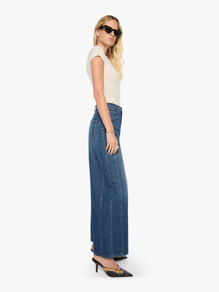 Side view of a woman in a mid blue super high-waisted barrel-leg jeans with a relaxed fit, zip fly, inset panels on the outer seams, long 31-inch inseam and a clean hem. 