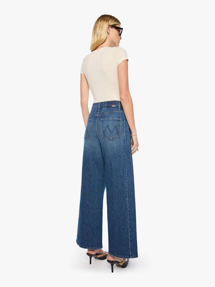 Back view of a woman in a mid blue super high-waisted barrel-leg jeans with a relaxed fit, zip fly, inset panels on the outer seams, long 31-inch inseam and a clean hem. 