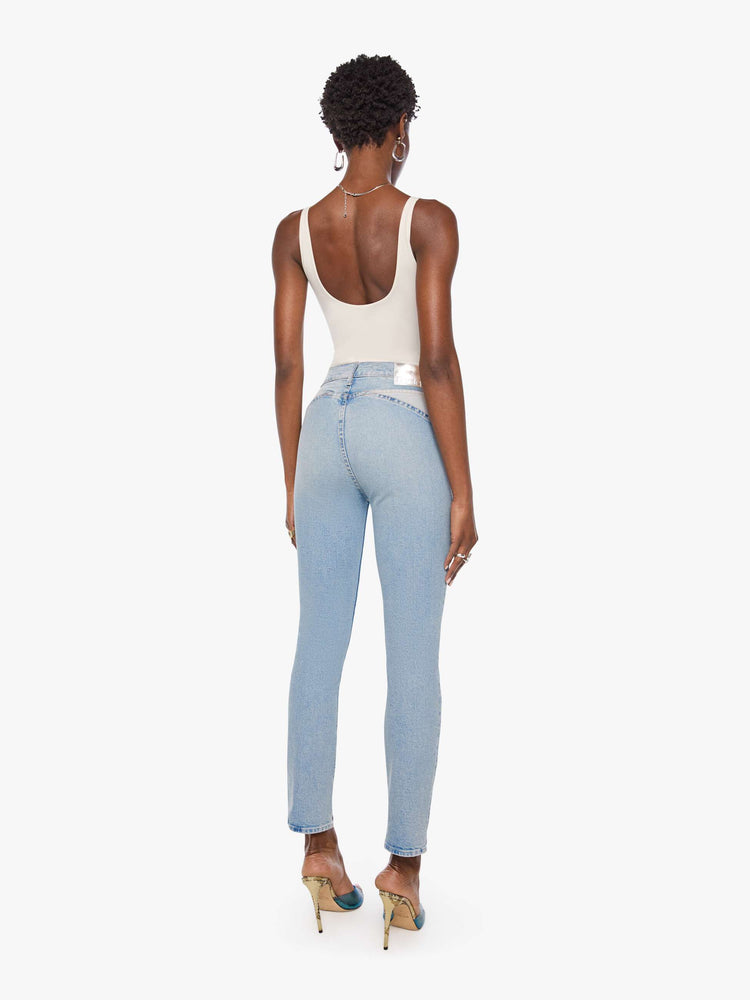 Back view of a woman in a light blue high-rise jean has a straight leg, zip fly, angled contrast cut-outs at the hips, a 29-inch inseam and a clean hem.