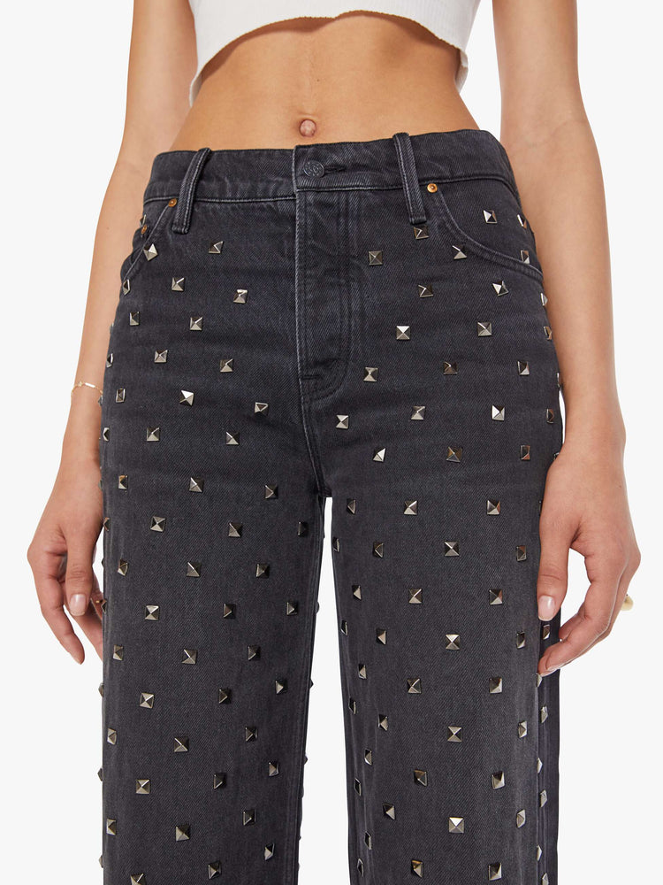 Front close up view of a woman wearing faded black denim pants with square studs throughout.