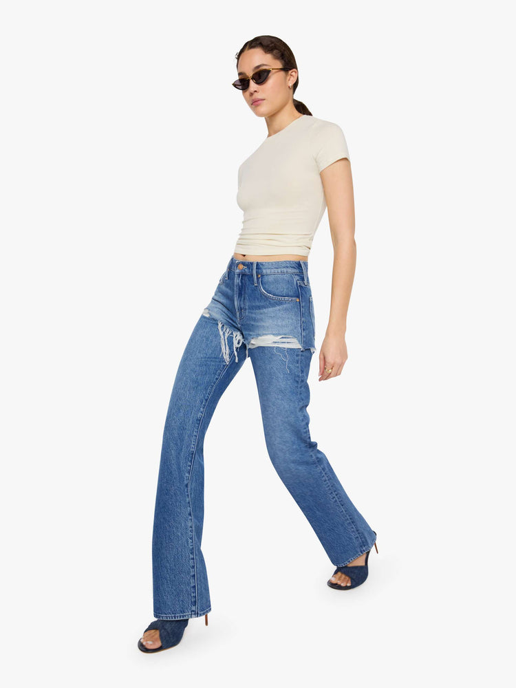 Walking view of a woman in a lower-rise jeans are designed to look like a pair of frayed shorts is layered on top, and are designed with a zip fly, narrow straight-leg, long 34-inch inseam and a clean hem.
