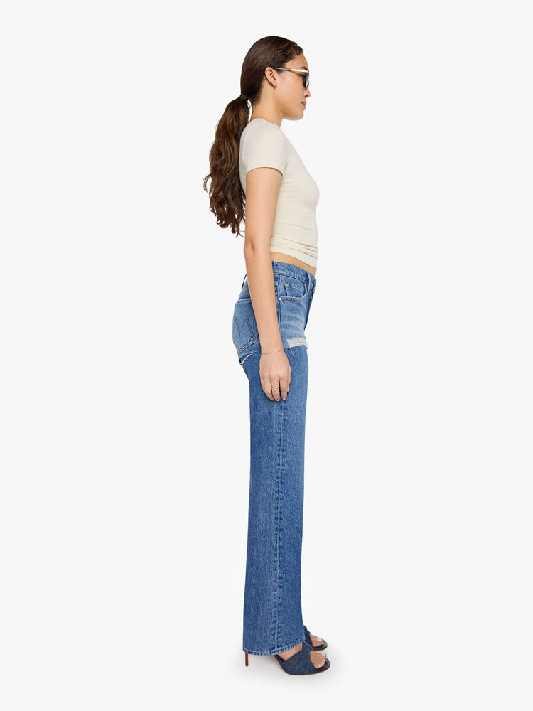 Side view of a woman in a lower-rise jeans are designed to look like a pair of frayed shorts is layered on top, and are designed with a zip fly, narrow straight-leg, long 34-inch inseam and a clean hem.