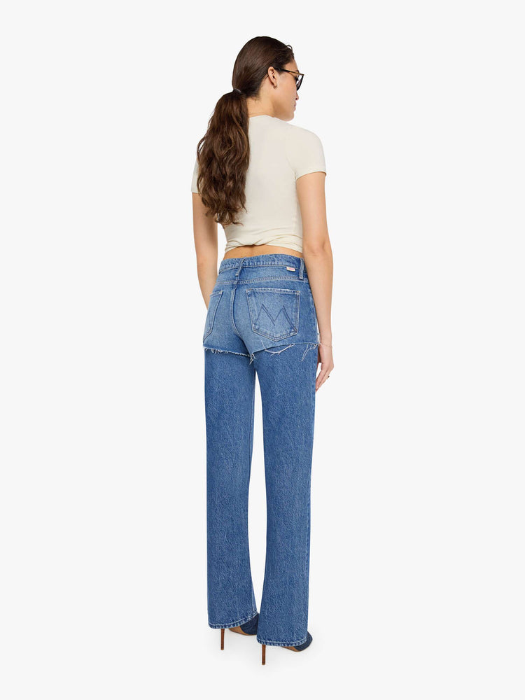 Back view of a woman in a lower-rise jeans are designed to look like a pair of frayed shorts is layered on top, and are designed with a zip fly, narrow straight-leg, long 34-inch inseam and a clean hem.