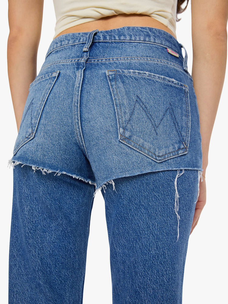 Close up view of a woman in a lower-rise jeans are designed to look like a pair of frayed shorts is layered on top, and are designed with a zip fly, narrow straight-leg, long 34-inch inseam and a clean hem.