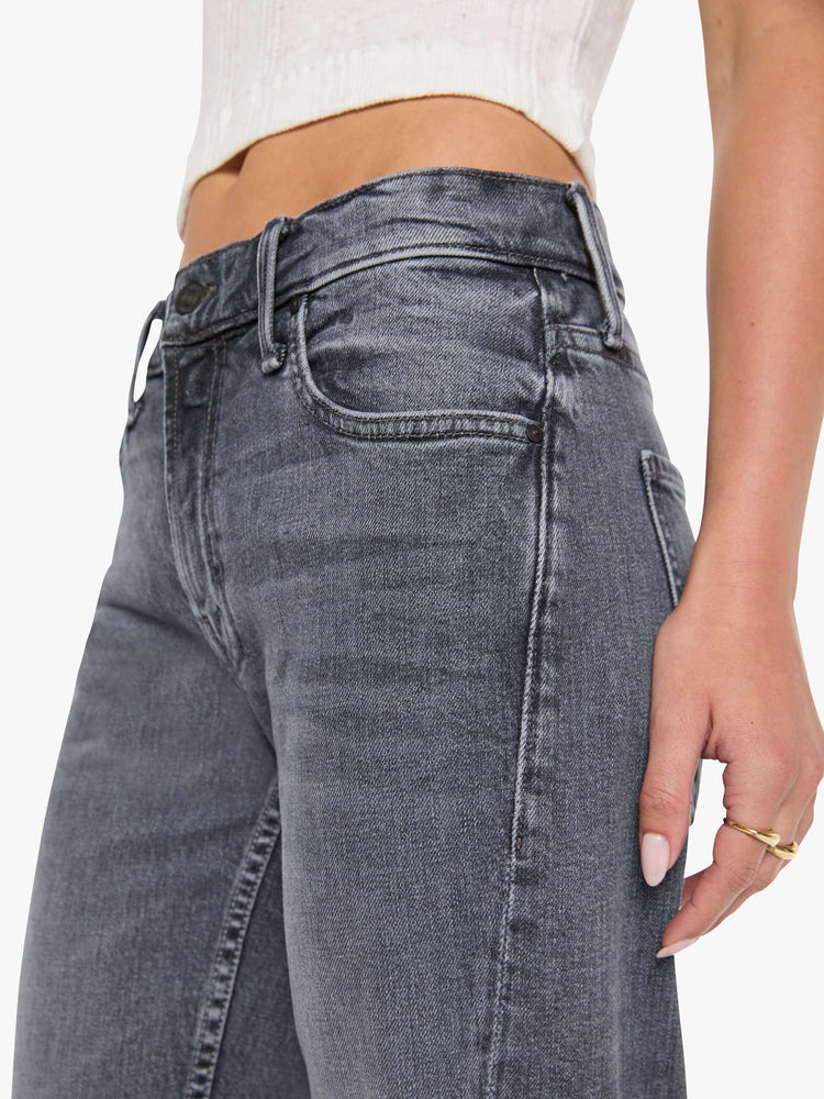 Close up view of a woman in a washed grey mid-rise bootcut with a zip fly, looser leg, twisted outer seam and a long 32-inch inseam with a clean hem.