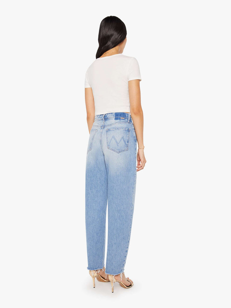 Back view of a woman in a light blue high-waisted jeans with a wide barrel leg, zip fly and a 29-inch inseam with a frayed hem.