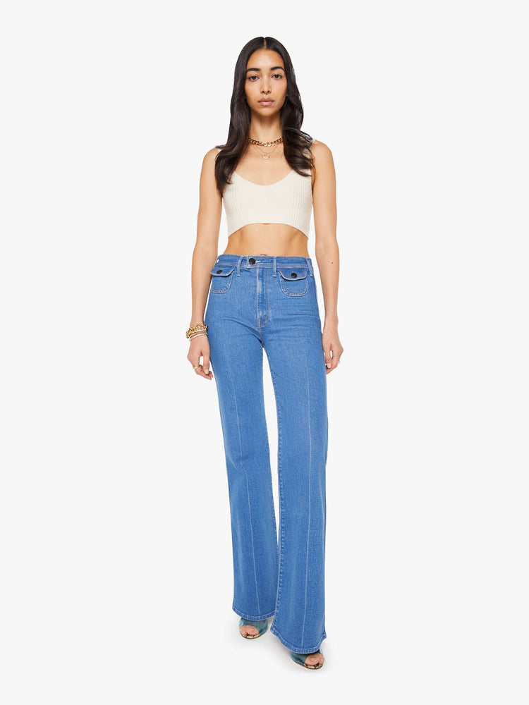 Front view of a woman in a mid blue wide leg jean features a high rise, buttoned waistband, zip fly, small patch pockets, long 32-inch inseam and a clean hem.