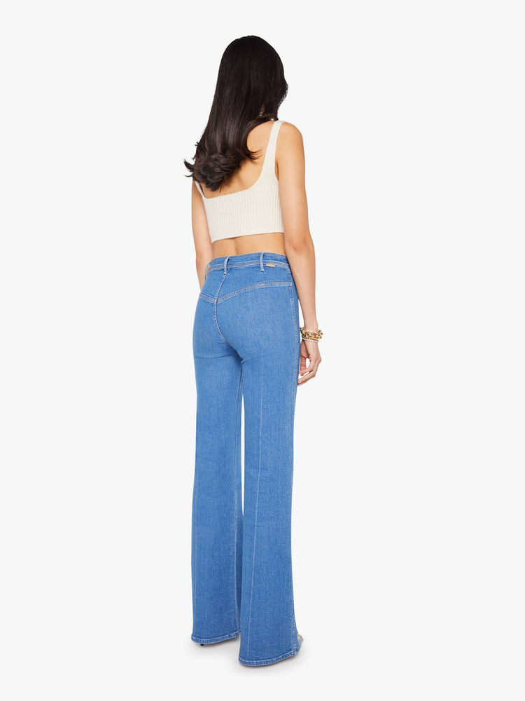 Back view of a woman in a mid blue wide leg jean features a high rise, buttoned waistband, zip fly, small patch pockets, long 32-inch inseam and a clean hem.