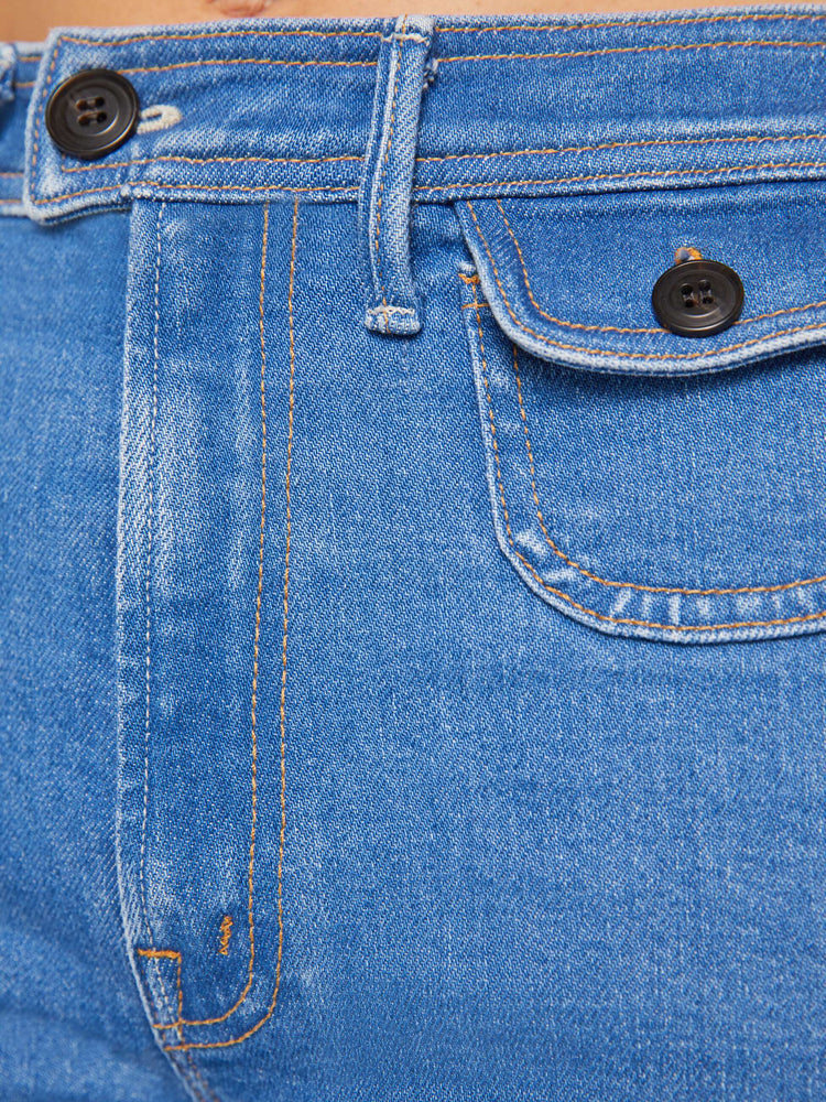 Swatch view of a woman in a mid blue wide leg jean features a high rise, buttoned waistband, zip fly, small patch pockets, long 32-inch inseam and a clean hem.