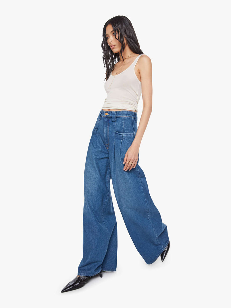Walking view of a woman in a super high rise wide-leg jeans are designed with slit pockets, pleated details, a zip fly and a long 31-inch inseam with a clean hem.