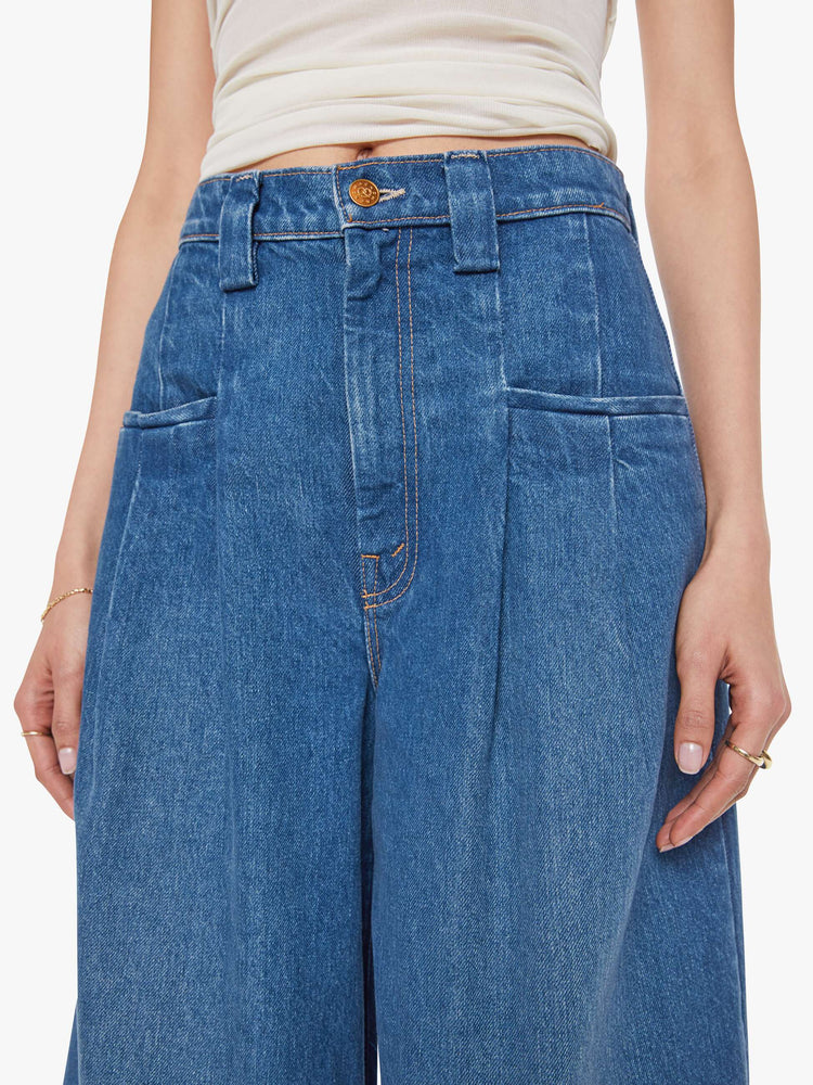 Close up view of a woman in a super high rise wide-leg jeans are designed with slit pockets, pleated details, a zip fly and a long 31-inch inseam with a clean hem.