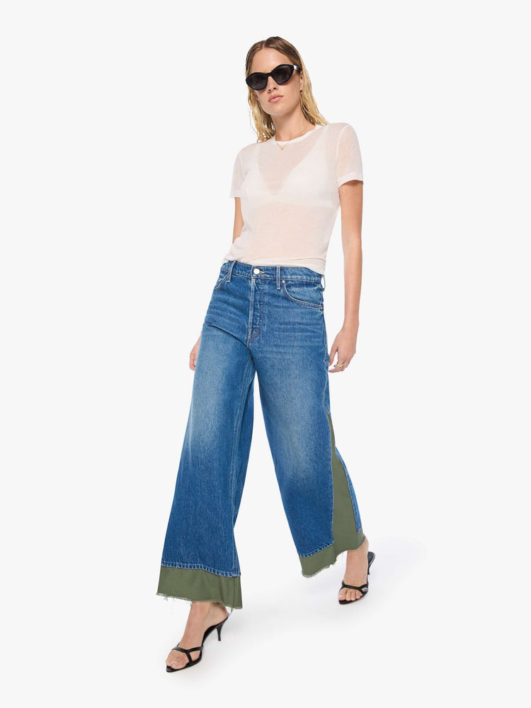 Walking view of a woman in a mid blue with green panels high-waisted jeans are designed with a button fly, low-slung fit, 30-inch inseam, a loose wide leg with inset panels on the outer seams and a frayed hem.