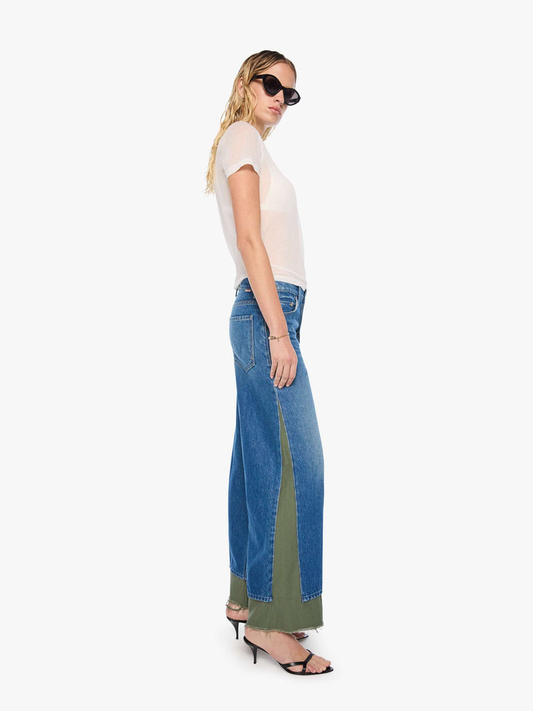 Side view of a woman in a mid blue with green panels high-waisted jeans are designed with a button fly, low-slung fit, 30-inch inseam, a loose wide leg with inset panels on the outer seams and a frayed hem.