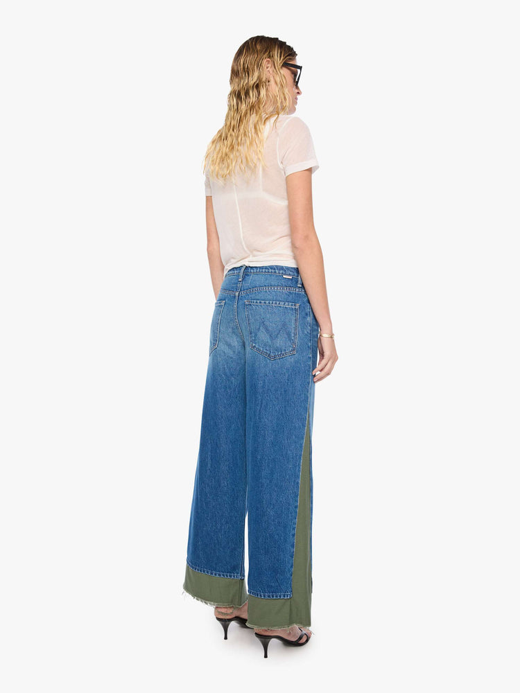 Back view of a woman in a mid blue with green panels high-waisted jeans are designed with a button fly, low-slung fit, 30-inch inseam, a loose wide leg with inset panels on the outer seams and a frayed hem.