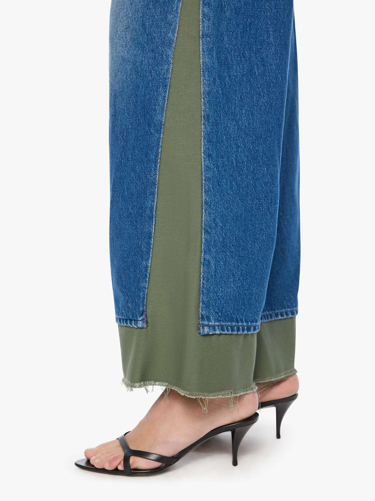 Hem close up view of a woman in a mid blue with green panels high-waisted jeans are designed with a button fly, low-slung fit, 30-inch inseam, a loose wide leg with inset panels on the outer seams and a frayed hem.