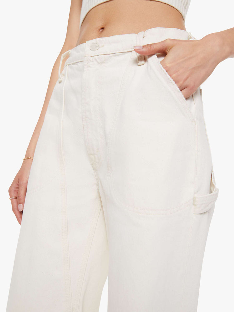 Close up view of a woman in a creamy white wide-leg jeans with a super high rise, zip fly, utility-inspired patch pockets, a hammer loop, angled seamed details across the front and a long 32-inch inseam with a clean hem.