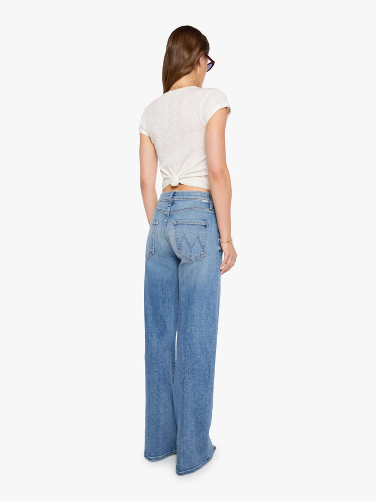 Back view of a woman in a mid blue wide-leg pants with a subtle barrel shape, a zip fly, mid rise and a 32-inch inseam with a clean hem.