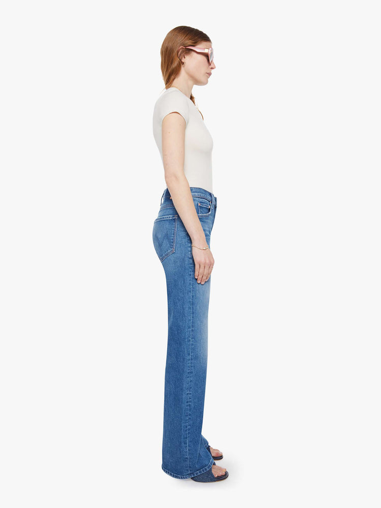 Side view of a woman in a med blue wide-leg pants with a zip fly, mid rise and a 32-inch inseam with a clean hem.