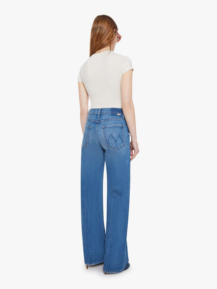 Back view of a woman in a med blue wide-leg pants with a zip fly, mid rise and a 32-inch inseam with a clean hem.