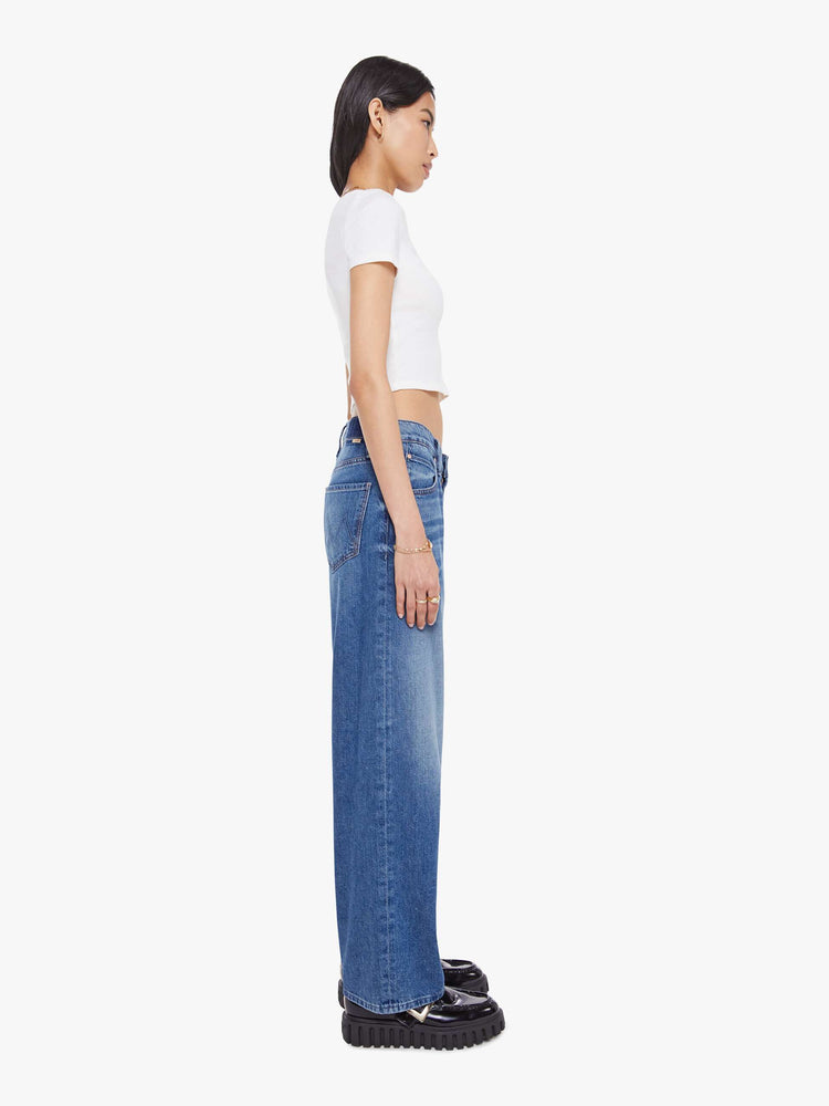 Side view of a woman in a mid blue   jeans designed to sit lower on the hips with a 28-inch inseam, zip fly, clean hem and slightly tapered leg. 