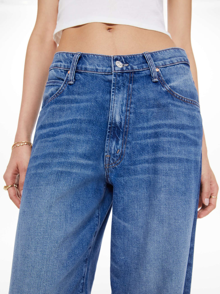 Close up view of a woman in a mid blue   jeans designed to sit lower on the hips with a 28-inch inseam, zip fly, clean hem and slightly tapered leg. 