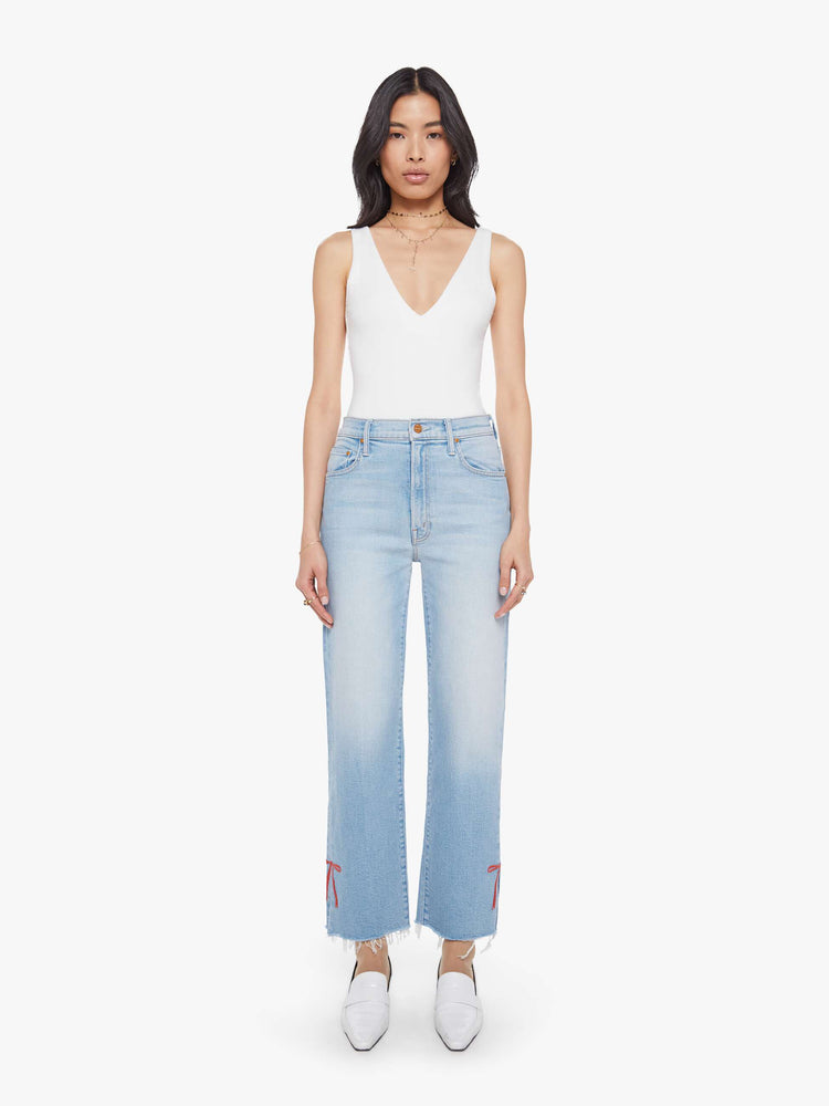 Front view of a woman in light blue high-waisted jeans with a straight leg, zip fly and a cropped 29-inch inseam with a sliced outer seam and a frayed hem.