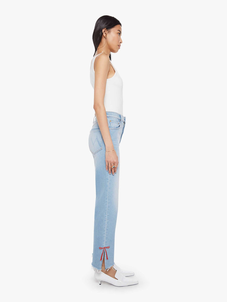 Side view of a woman in light blue high-waisted jeans with a straight leg, zip fly and a cropped 29-inch inseam with a sliced outer seam and a frayed hem.