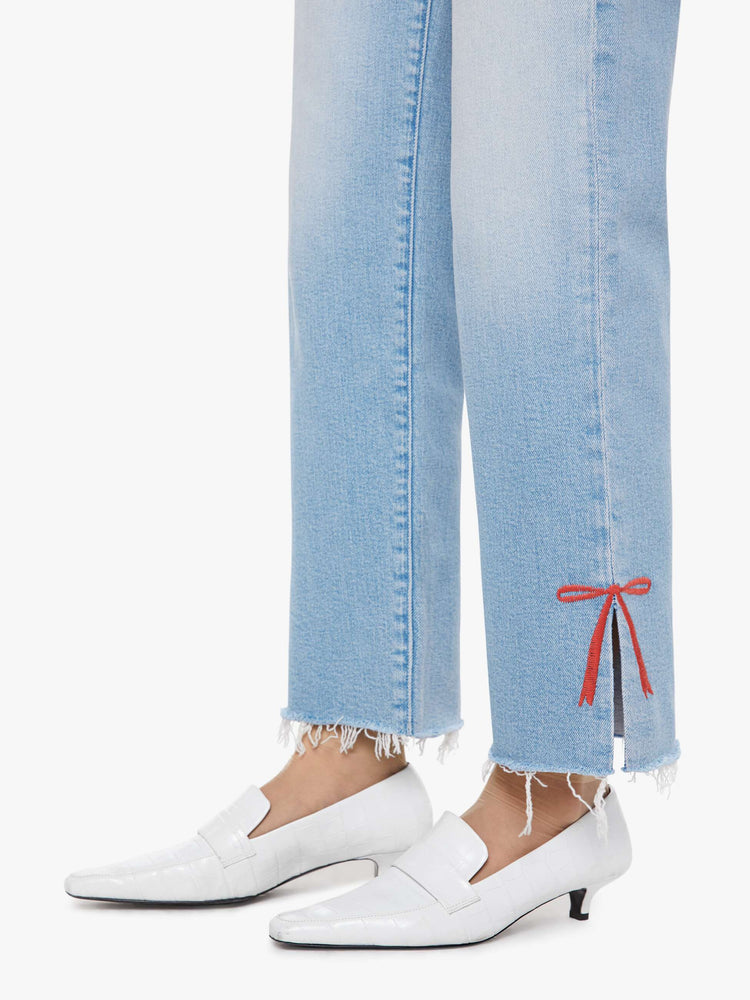 Hem view of a woman in light blue high-waisted jeans with a straight leg, zip fly and a cropped 29-inch inseam with a sliced outer seam and a frayed hem.