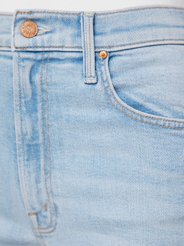 Hem view of a woman in light blue high-waisted jeans with a straight leg, zip fly and a cropped 29-inch inseam with a sliced outer seam and a frayed hem.
