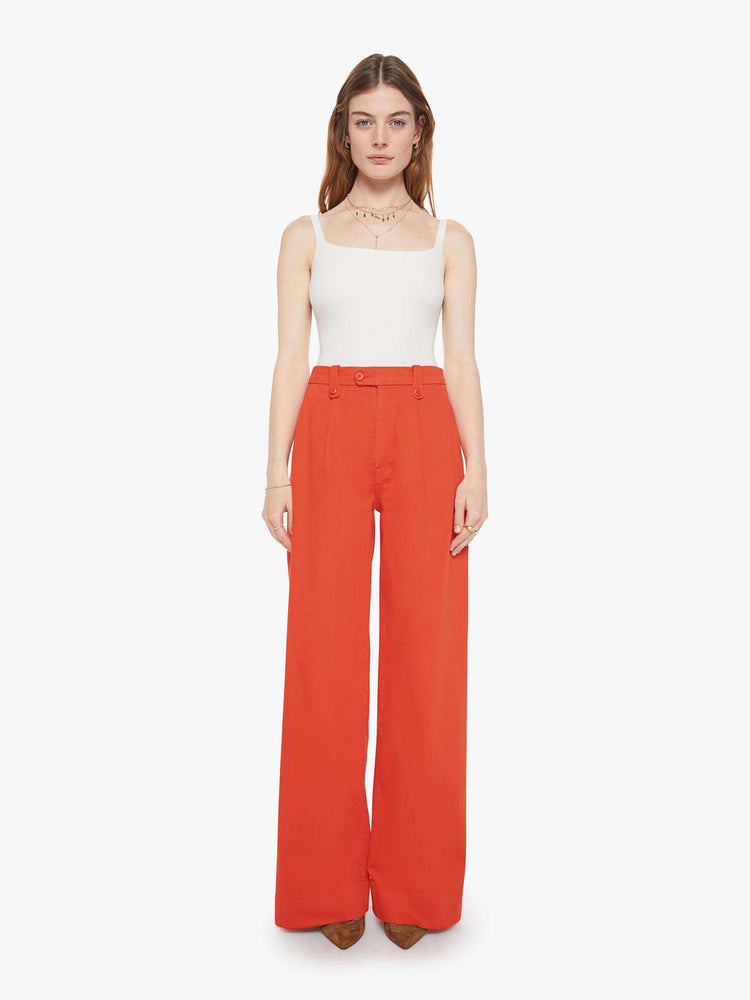 Front view of a woman in a bight orange trouser-inspired jeans with a high rise, wide leg, zip fly, pleated waistband, slit pockets and a long 31-inch inseam with a clean hem.