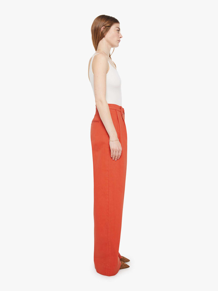 Side view of a woman in a bight orange trouser-inspired jeans with a high rise, wide leg, zip fly, pleated waistband, slit pockets and a long 31-inch inseam with a clean hem.