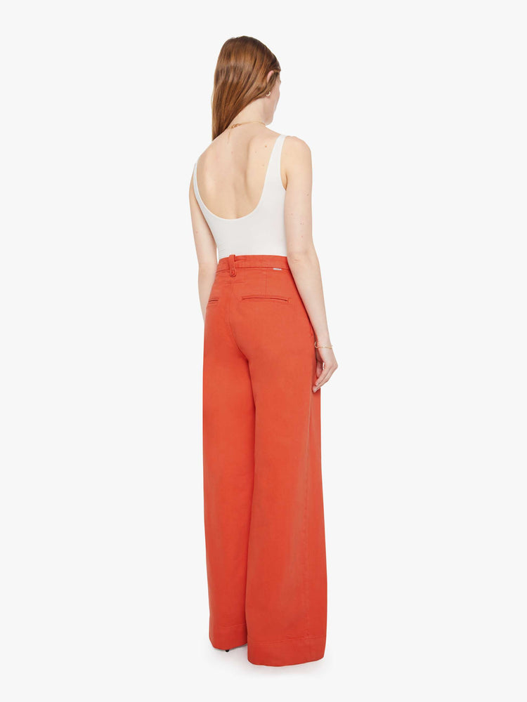 Back view of a woman in a bight orange trouser-inspired jeans with a high rise, wide leg, zip fly, pleated waistband, slit pockets and a long 31-inch inseam with a clean hem.