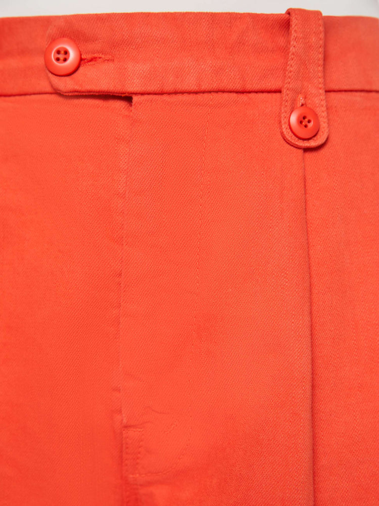 Close up view of a woman in a bight orange trouser-inspired jeans with a high rise, wide leg, zip fly, pleated waistband, slit pockets and a long 31-inch inseam with a clean hem.