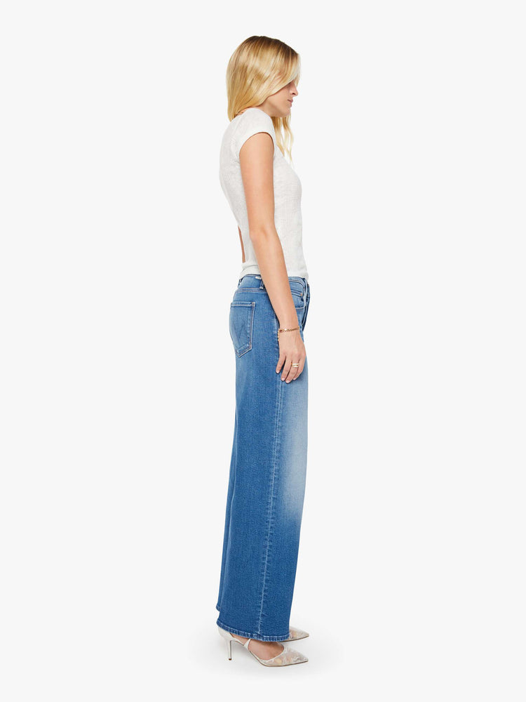 Side view of a woman in a mid blue high-waisted wide leg jeans with a button fly, a long 32-inch inseam and loose, low-slung fit.