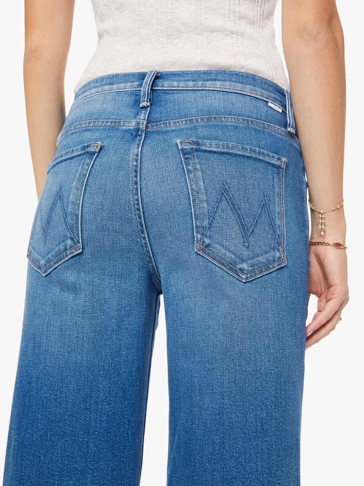 Back close up view of a woman in a mid blue high-waisted wide leg jeans with a button fly, a long 32-inch inseam and loose, low-slung fit.