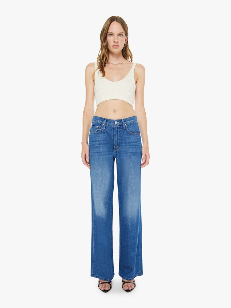 Front view of a woman in med blue mid-rise jeans with a loose fit, wide leg, zip fly and a 31-inch inseam with a clean hem.