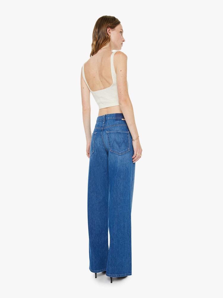 Back view of a woman in med blue mid-rise jeans with a loose fit, wide leg, zip fly and a 31-inch inseam with a clean hem.