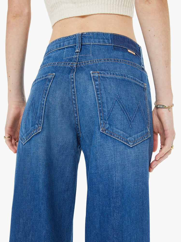 Close up view of a woman in med blue mid-rise jeans with a loose fit, wide leg, zip fly and a 31-inch inseam with a clean hem.