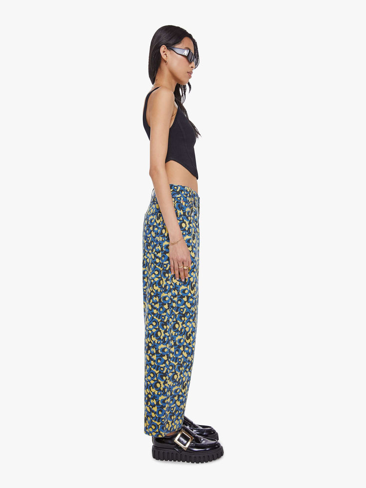 Side view of a woman in lower on the hips  jean with an ankle-length inseam, zip fly, clean hem and slightly tapered leg in a a blue, yellow and black leopard print.